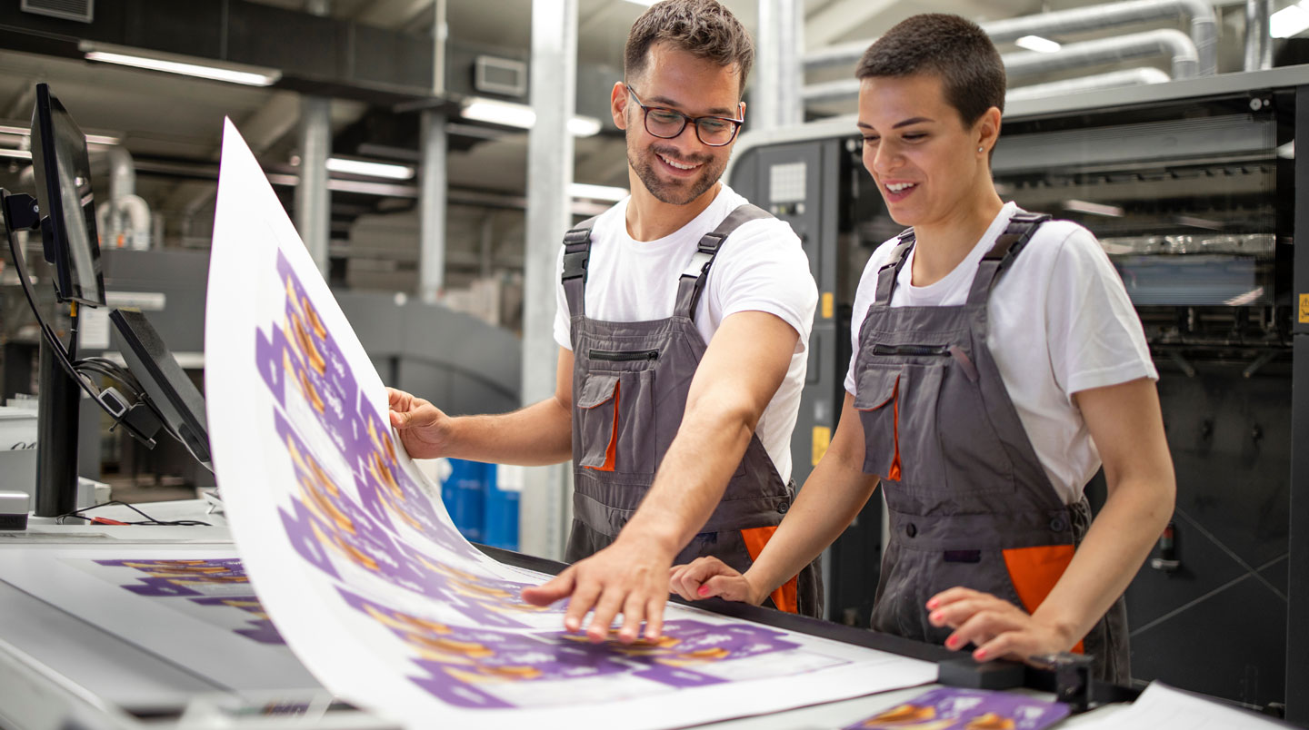 Responsable marketing examinant des supports PLV (roll-up et flyers) sur une table de travail lors de la préparation d'un salon professionnel